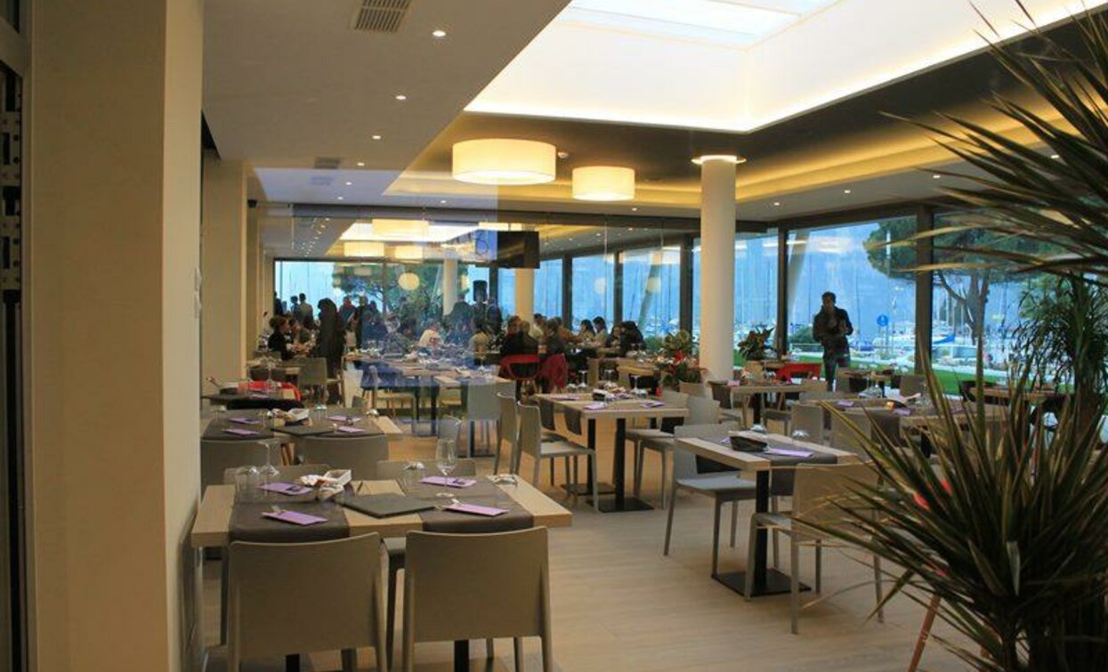 Un ristorante moderno con tavoli ben apparecchiati e ampie vetrate. Molti clienti stanno socializzando in un ambiente elegante e luminoso.